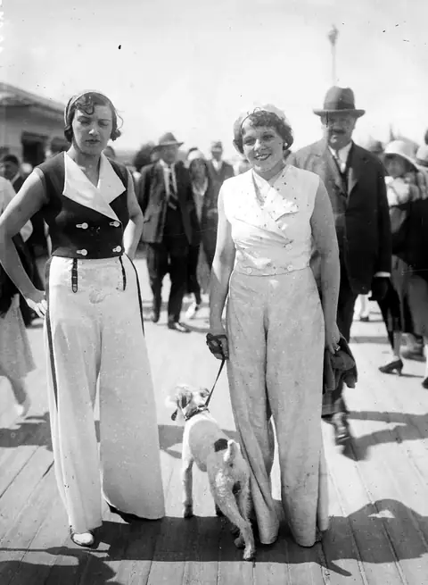 Two women in wide trousers walking a dog on the Deauville boardwalk, 1931